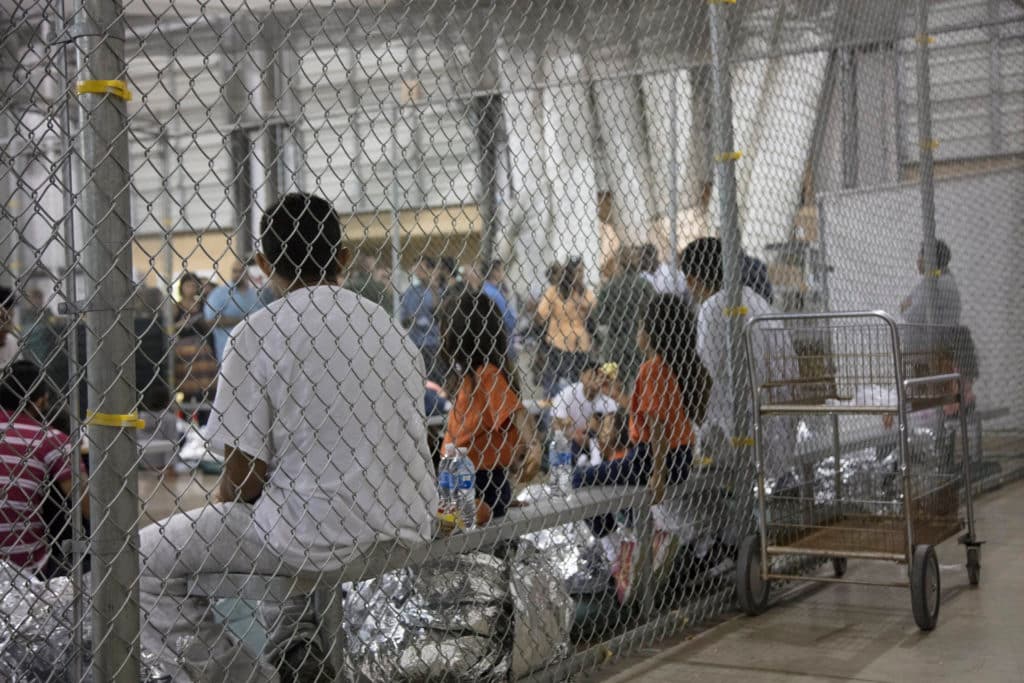 People wrapped in mylar blankets sit inside a chain-link enclosure in a U.S. detention facility.