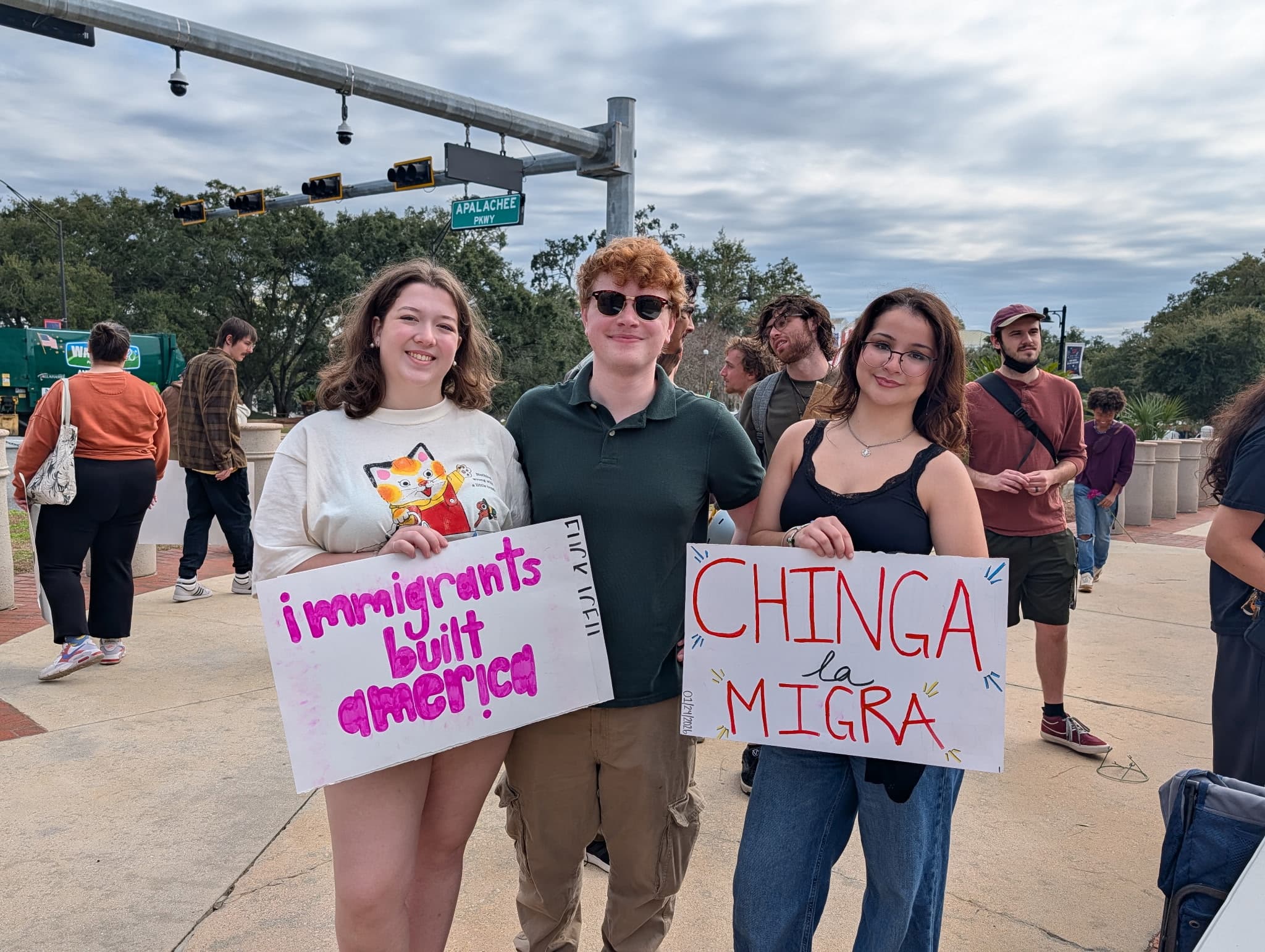 Three people with handmade signs supporting immigrants at a demonstration.