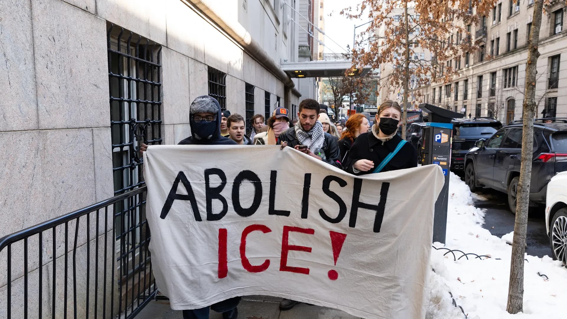 Protesters in a city street hold a large 'Abolish ICE!' banner.