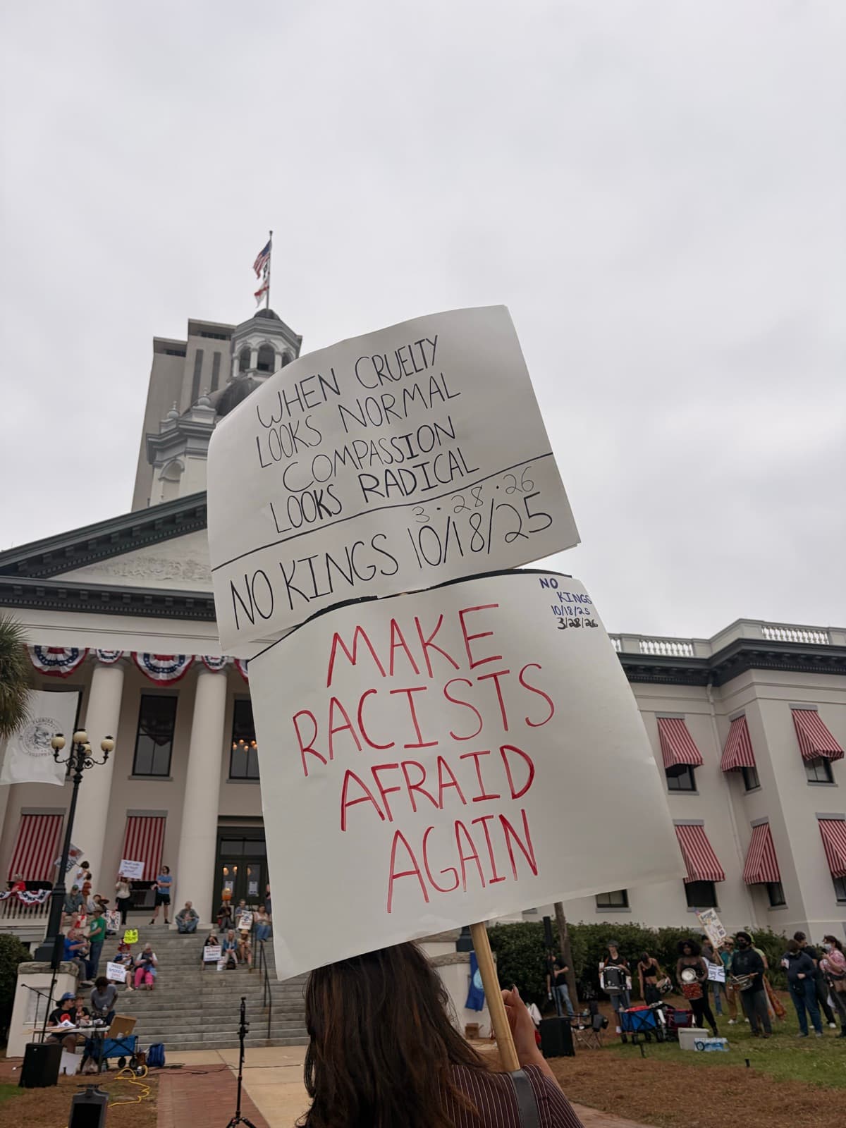 Daytime 'No Kings' rally at the Florida State Capitol with signs reading 'When cruelty looks normal, compassion looks radical' and 'Make racists afraid again.'